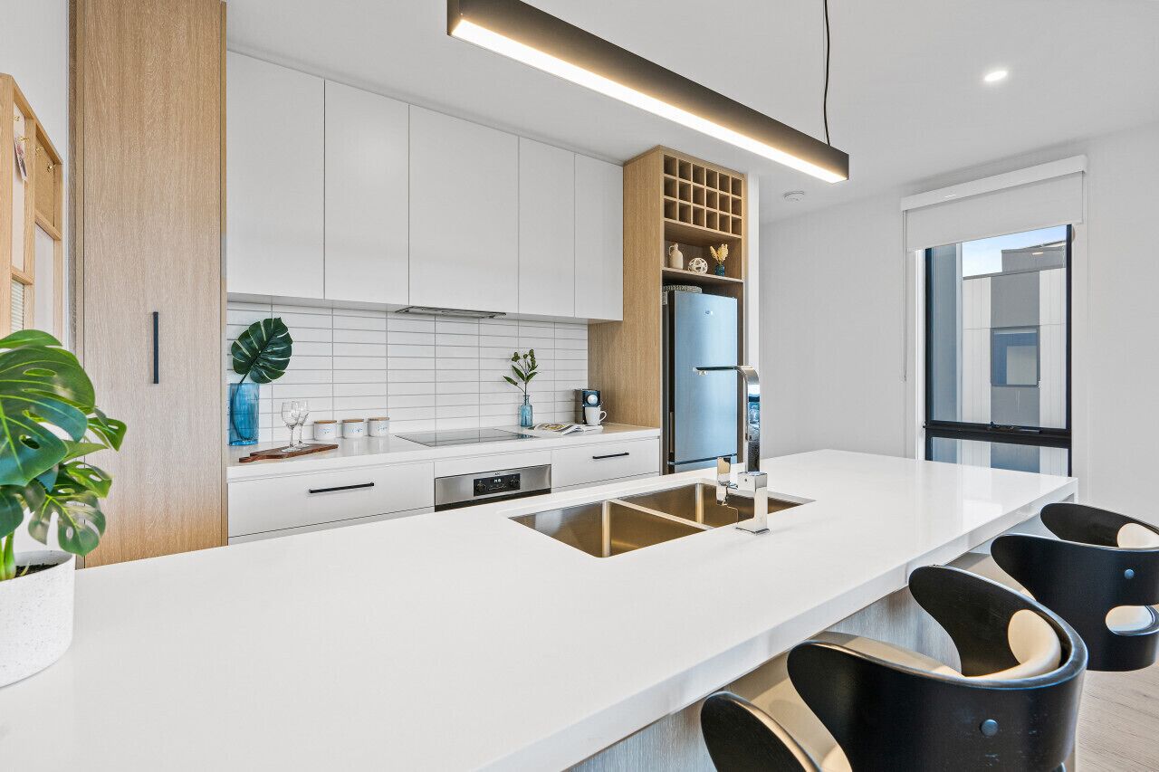 A modern kitchen with white cabinetry, a built-in sink, and black bar stools.