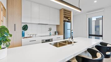 A modern kitchen with white cabinetry, a built-in sink, and black bar stools.