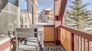 A balcony with a wooden railing, a chair, and a view of snow-covered buildings and a tree. - First Tracks 2br 2bath Steamboat Heaven (Steamboat Springs)