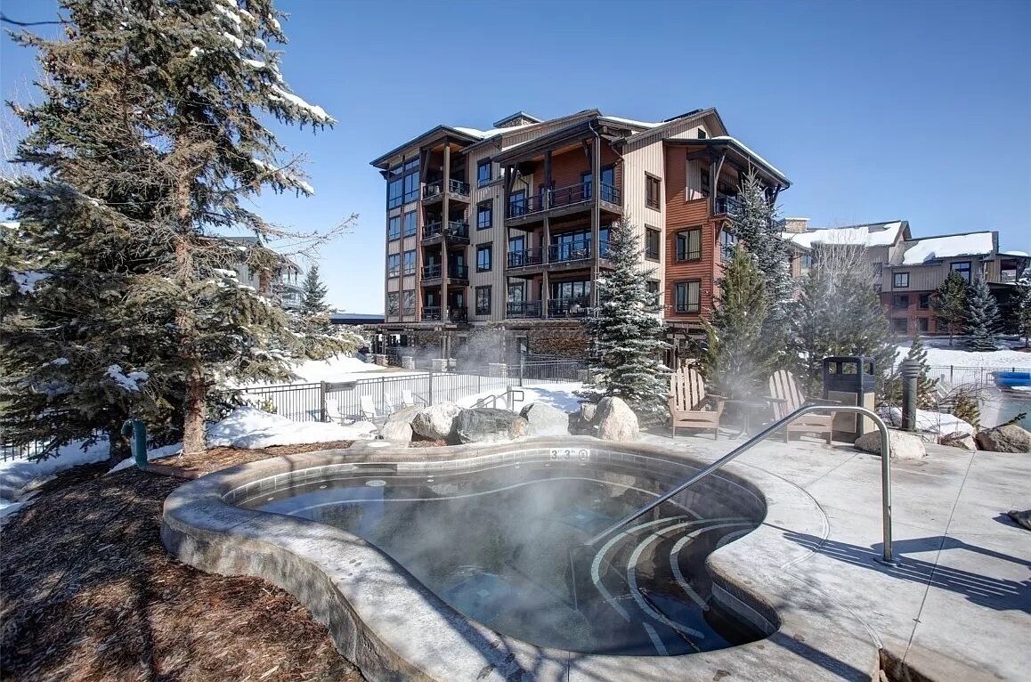 A hot tub surrounded by a stone deck, with a multi-story building in the background.