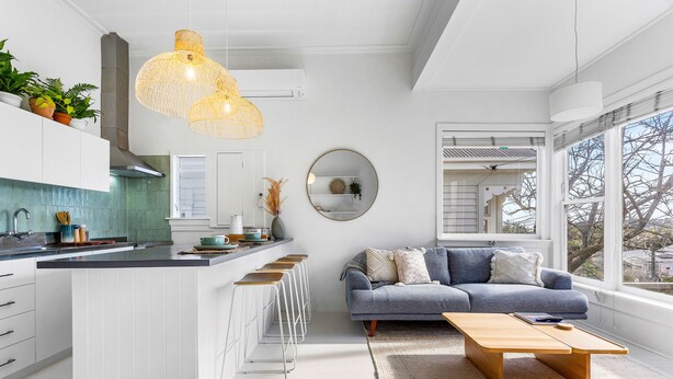 A modern kitchen with white cabinetry, a central island with bar stools, and a large window providing a view of the outdoors. - Grey Lynn Villa - Short Walk to Ponsonby Central (Auckland)