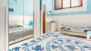 A bedroom with a bed, a dresser, a nightstand, a mirror, and a window with blinds. - GuestHost - Bright 62sqm apartment, ideal for 3 people, located on the ground floor of a building WITHOUT a lift (two flights of stairs to access it).The accommodation is located in the La Collina residence, in Villasimius, in about 13 minutes by car y (Villasimius)