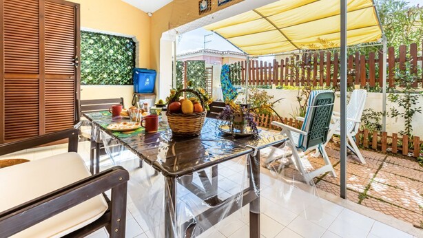 A patio with a table, chairs, and a yellow canopy. - GuestHost - Bright 62sqm apartment, ideal for 3 people, located on the ground floor of a building WITHOUT a lift (two flights of stairs to access it).The accommodation is located in the La Collina residence, in Villasimius, in about 13 minutes by car y (Villasimius)