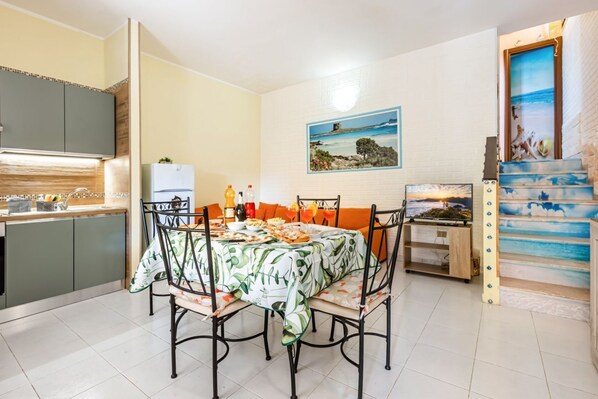 A dining area with a table set for four, a kitchen with grey cabinets, and a staircase with a beach mural.