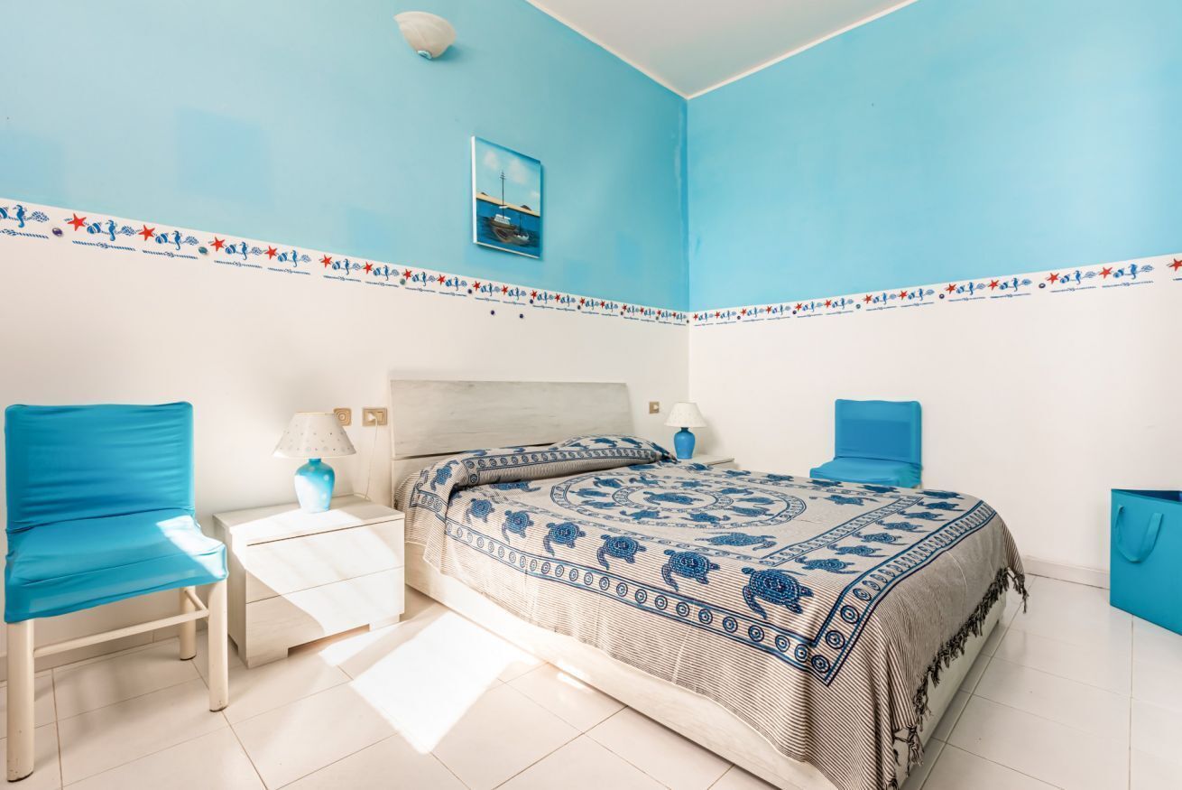 Ein Schlafzimmer mit einem Bett, zwei Stühlen, einem Nachttisch, einer Lampe und einer Wand mit dekorativer Bordüre.