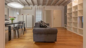 Una sala de estar con sofá, una mesa de comedor con sillas, una estantería y un radiador.
