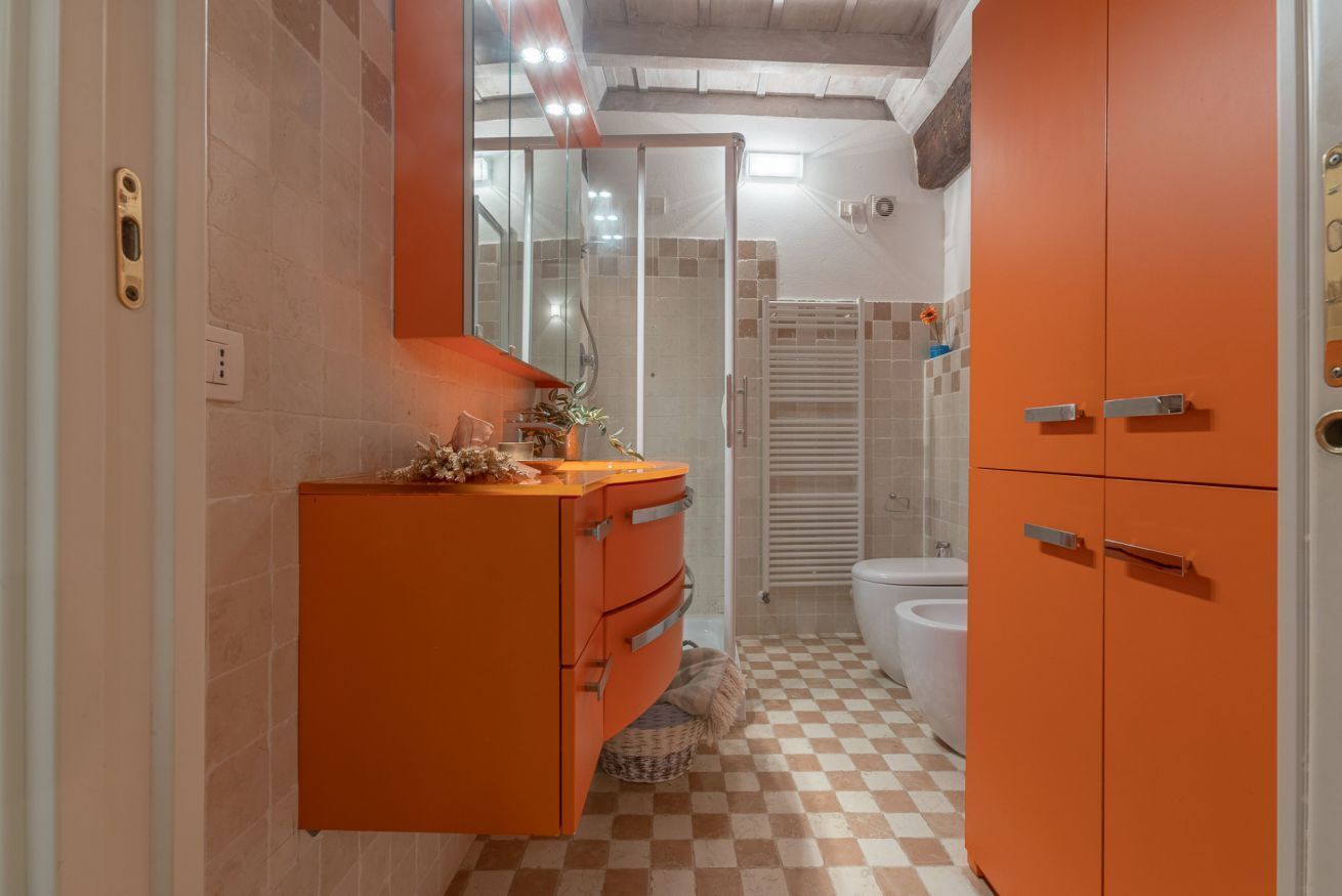 Een badkamer met een geruite vloer, een wit toilet, een oranje kastje en een douchecabine met glazen wanden.