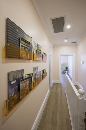 A hallway with a wall-mounted display of magazines and books, a white railing, and a door leading to another room. - Where Barbie Lives by Glass Et Cetera (Chippendale)