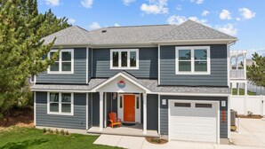 Une maison à deux étages avec un garage, une véranda et un petit jardin devant.