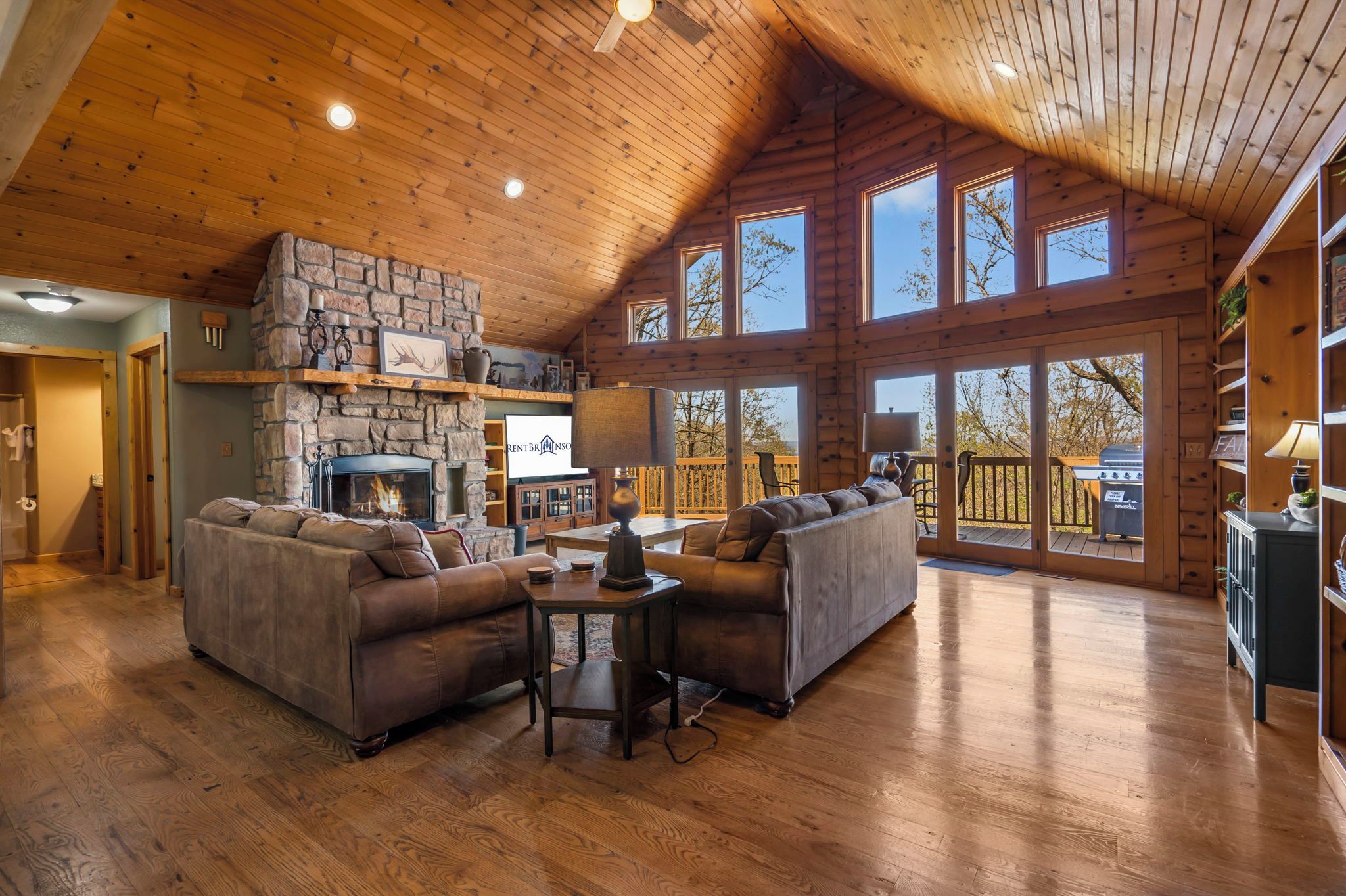 A spacious living room with a stone fireplace, two sofas, and a wooden ceiling.