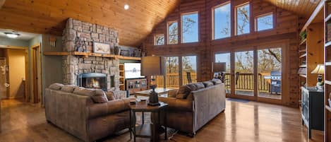 A spacious living room with a stone fireplace, two sofas, and a wooden ceiling.