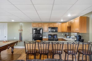 A kitchen with wooden cabinets, a refrigerator, a microwave, and a stove. There is a pool table and chairs in the adjacent room. - Rustic Lakeview Cabin Escape featuring Billiards, Free Daily Attraction Tickets & Close to Big Cedar (Ridgedale)