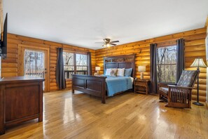 Une chambre à coucher située dans une cabane en rondins, avec un lit, une table de chevet, une lampe, une chaise et un ventilateur de plafond.