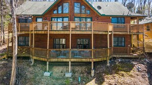 Une cabane en rondins à deux étages, dotée d’un balcon et entourée d’arbres.