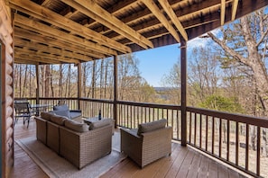 A covered outdoor seating area with wicker furniture and a view of the surrounding forest. - Rustic Lakeview Cabin Escape featuring Billiards, Free Daily Attraction Tickets & Close to Big Cedar (Ridgedale)
