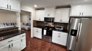 A kitchen with white cabinets, a stainless steel refrigerator, a microwave, an oven, and a toaster. - YOUPON DRIVE (Galveston)