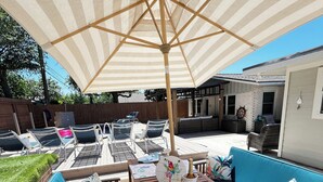 A patio area with a wooden table, blue cushioned seating, and a large striped umbrella. - YOUPON DRIVE (Galveston)