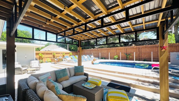 A covered outdoor seating area with wicker furniture and a pool in the background. - YOUPON DRIVE (Galveston)
