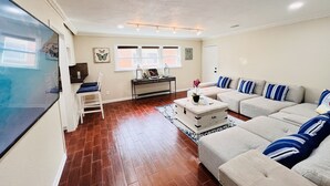 A living room with a beige sofa, a white armchair, a coffee table, and a TV. - YOUPON DRIVE (Galveston)