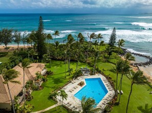 A resort with a swimming pool, lush greenery, and a view of the ocean.