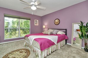 A bedroom with a large window, a ceiling fan, a bed with a pink and white bedspread, a bedside lamp, and a mirror. - Your home away from home! Pet friendly & 5 minutes from WEC. (Ocala)