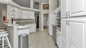 A modern kitchen with white cabinetry, a central island with stools, and a stainless steel trash can. - Your home away from home! Pet friendly & 5 minutes from WEC. (Ocala)