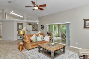 Ein geräumiges Wohnzimmer mit einer Ledersofa, einem Couchtisch und einem Deckenventilator.