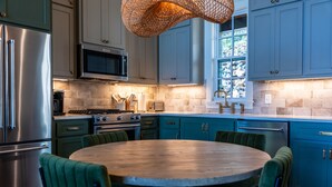 A modern kitchen with a round dining table, green upholstered chairs, and blue cabinets. - Lakeside Cottage in the Treetops - 2 bedrooms with amazing view (Jacksons' Gap)