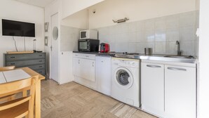 A compact kitchen with a microwave, toaster, and washing machine. There is a TV mounted on the wall and a small table with chairs. - Studio Crivelli - Welkeys (Hyères)