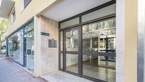A modern building entrance with glass doors, a visible address sign, and a small outdoor area with a bench. - Studio Crivelli - Welkeys (Hyères)