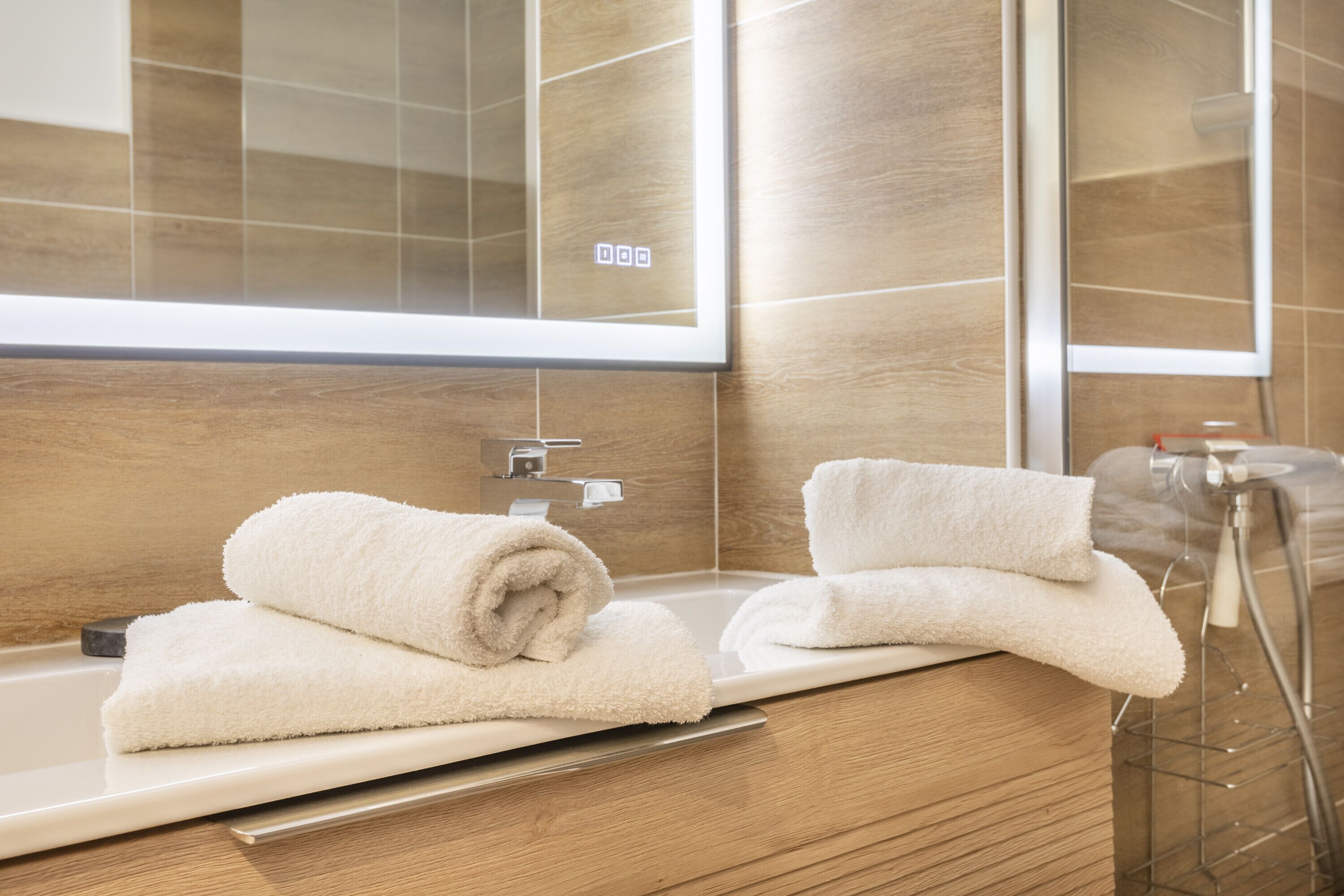 A modern bathroom with a wooden vanity, a large mirror, and two white towels on the sink.