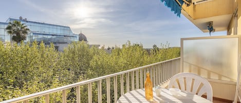 A balcony with a table and chairs, overlooking a lush garden and a modern building with a dome.