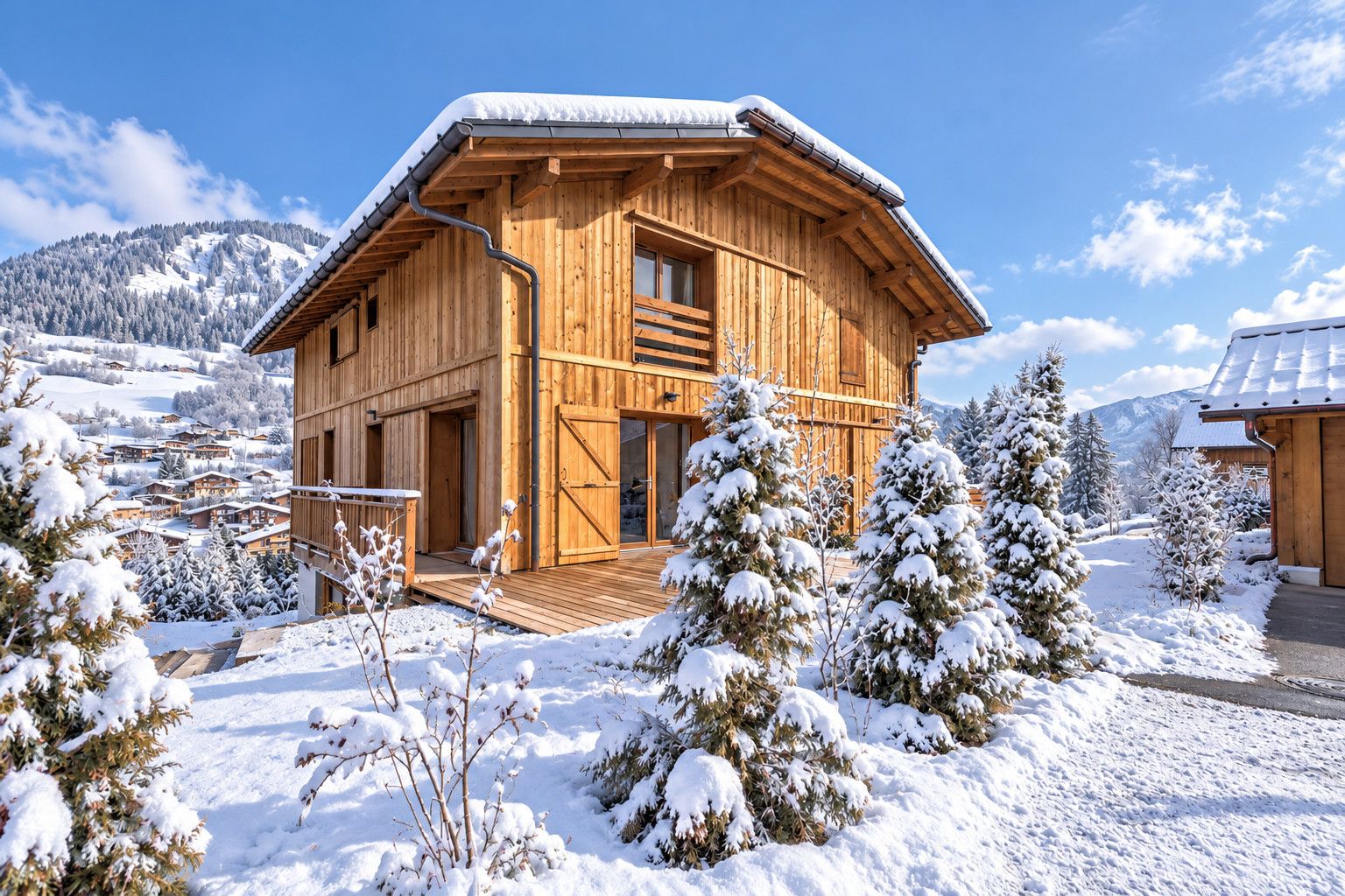 Un chalet en bois doté d’une terrasse en bois, entouré d’arbres et de montagnes couverts de neige.
