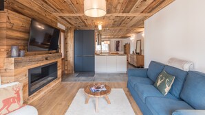 A modern living room with a wooden ceiling, a blue sofa, a coffee table, and a TV mounted on the wall.