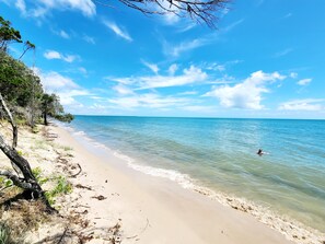 A beach with clear blue water, a sandy shore, and a person swimming. - Beach Shed Toogoom (Toogoom)