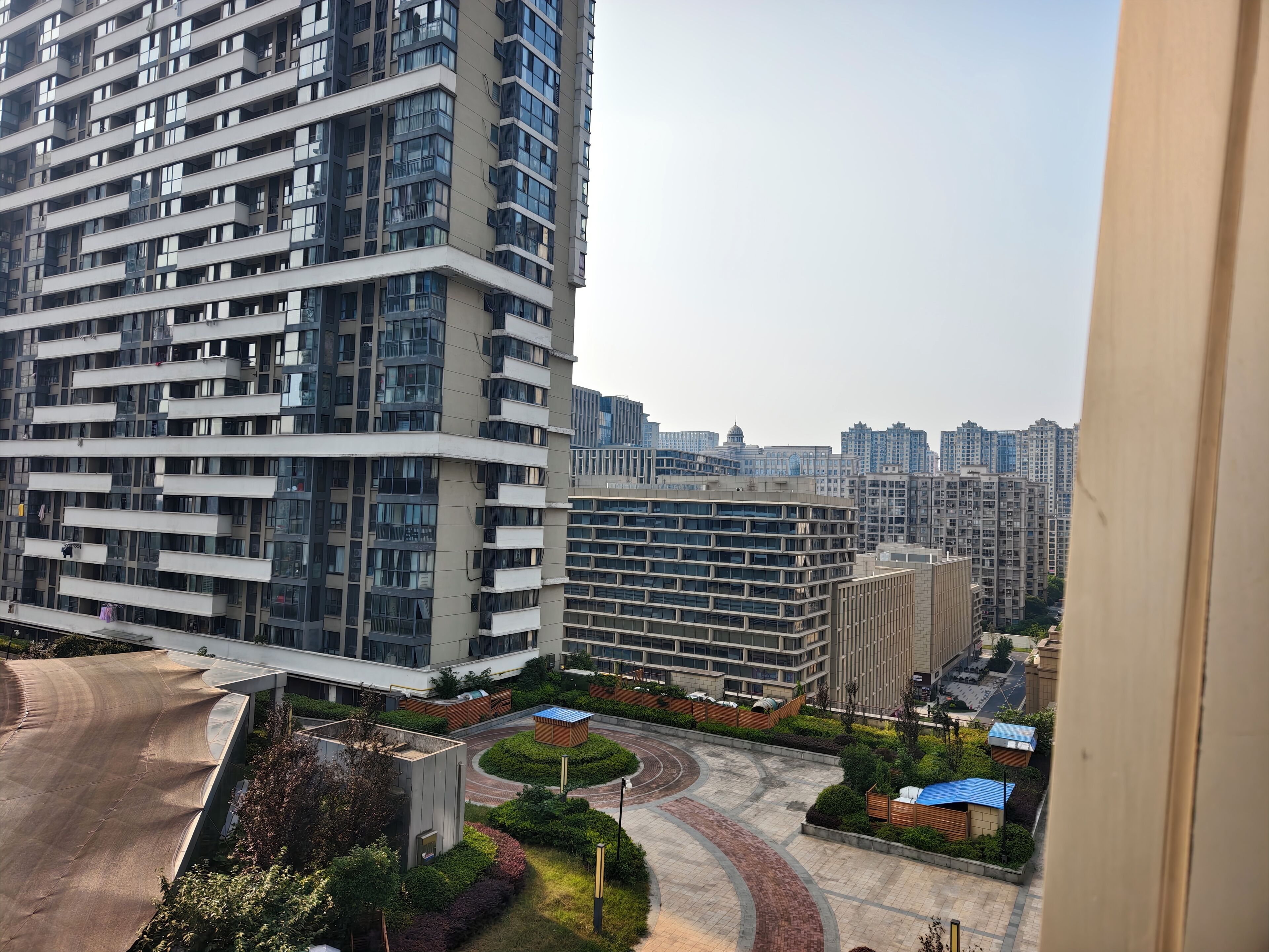 Un edificio residencial de gran altura con varios balcones, un patio central con vegetación y vistas a edificios altos circundantes.