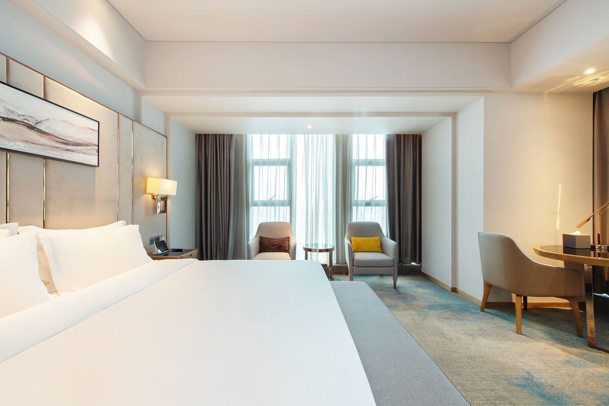 A hotel room with a large bed, two armchairs, a small table, and a desk.