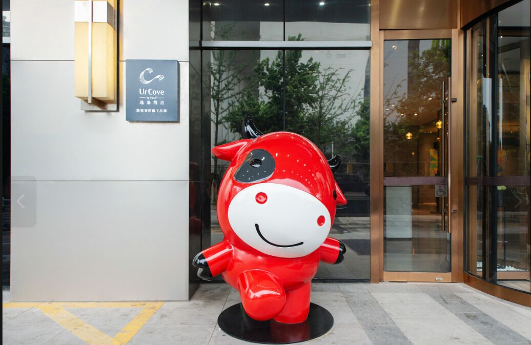 Una estatua roja de mascota frente a un edificio con un cartel que dice 'UrCove'.