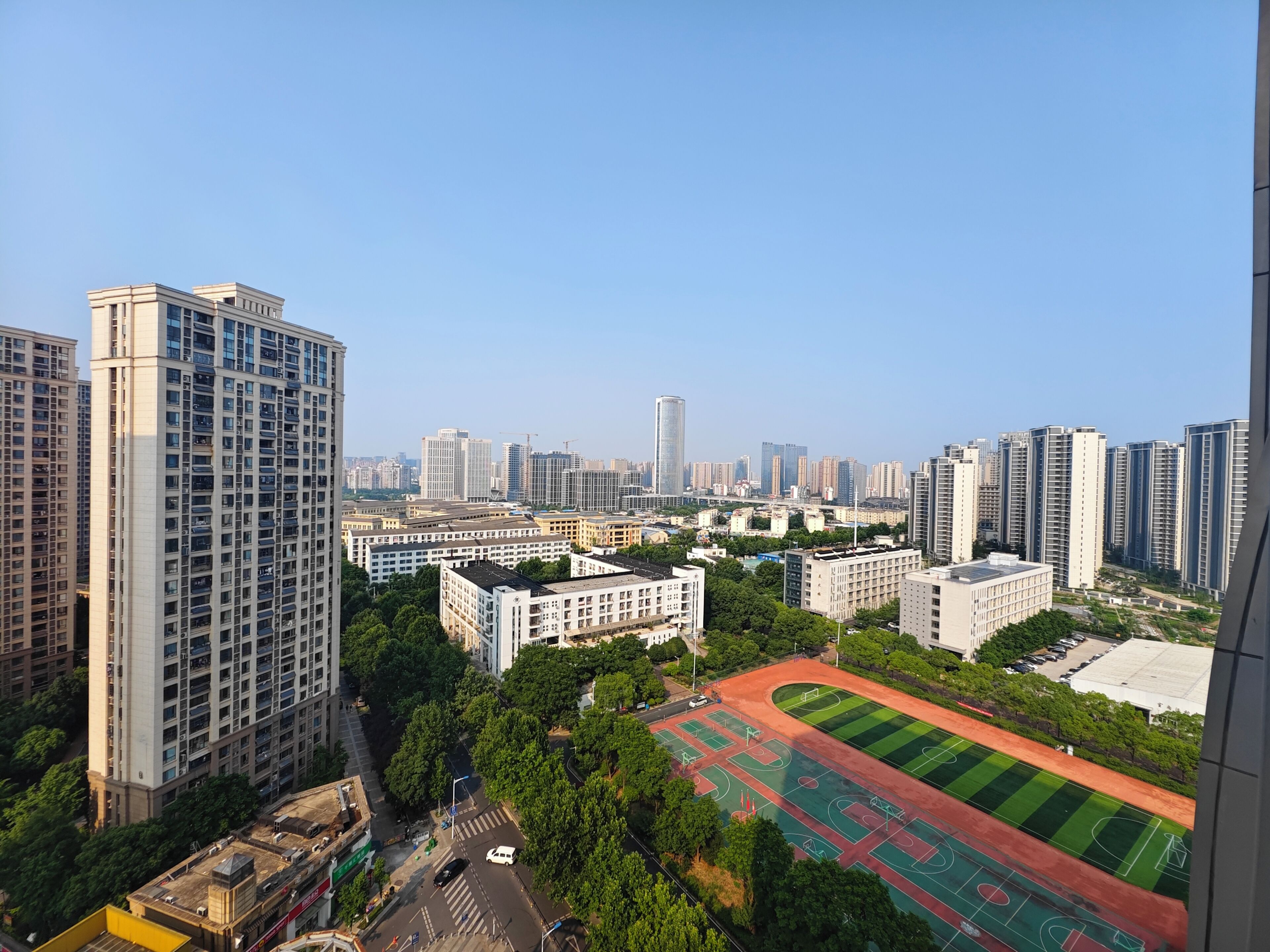 A high-rise building with a view of a cityscape, including other tall buildings and a sports field.