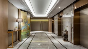 A modern hotel lobby with a marble floor, a reception desk, a painting, and elevators. - UrCove Hefei Eco-Tech Development Area (Hefei)