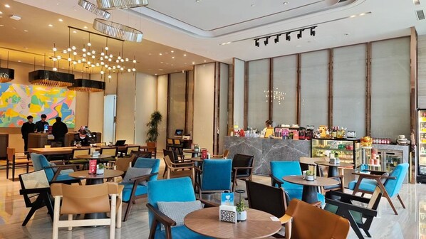 Un moderno vestíbulo de hotel con mesas redondas, sillas azules y marrones, una recepción y un área de bar con una exhibición de botellas.
