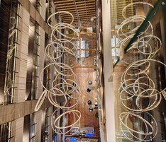 A high-ceiling atrium with a central open space, surrounded by glass railings and illuminated by circular light fixtures.