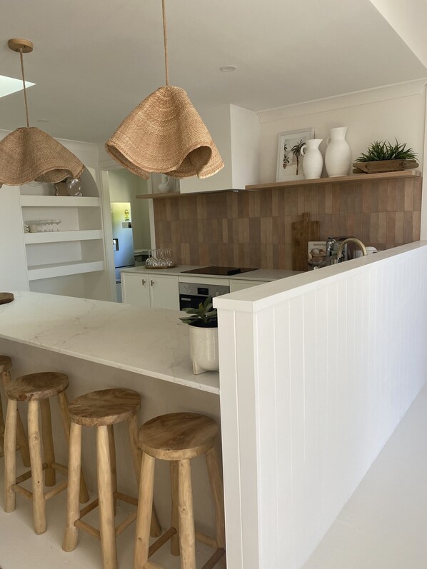 A modern kitchen with a central island, wooden stools, pendant lights, and a wooden backsplash.