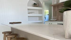A kitchen with a white countertop, wooden stools, and a hanging light fixture. - Mediterranean, coastal retreat in the heart of Toukley. (Toukley)