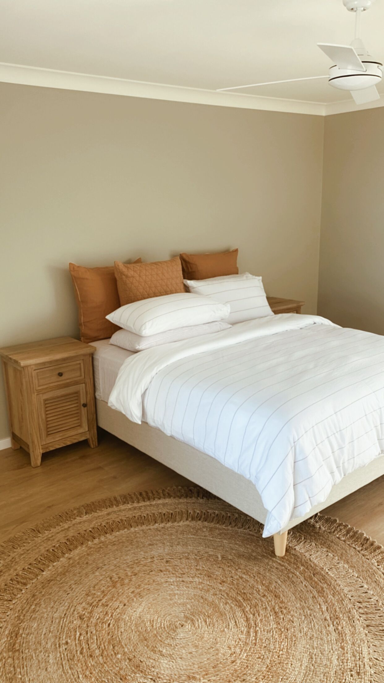 A bedroom with a bed, a nightstand, a ceiling fan, and a woven rug.