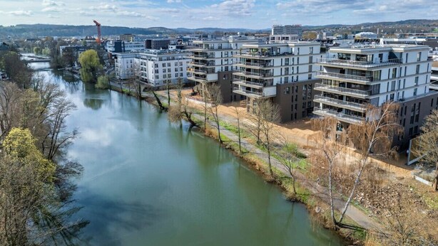 A modern apartment complex with multiple balconies, a river in the foreground, and a clear sky. - River Lux Suite | 5min to HBF (Wetzlar)