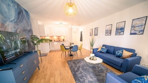 A modern living room with a blue sofa set, a dining area with yellow chairs, and a kitchen in the background. - River Lux Suite | 5min to HBF (Wetzlar)