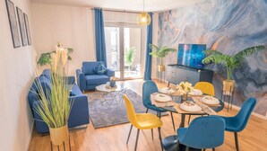 A modern living room with a sofa, dining table, and chairs, a TV, and a large window. - River Lux Suite | 5min to HBF (Wetzlar)