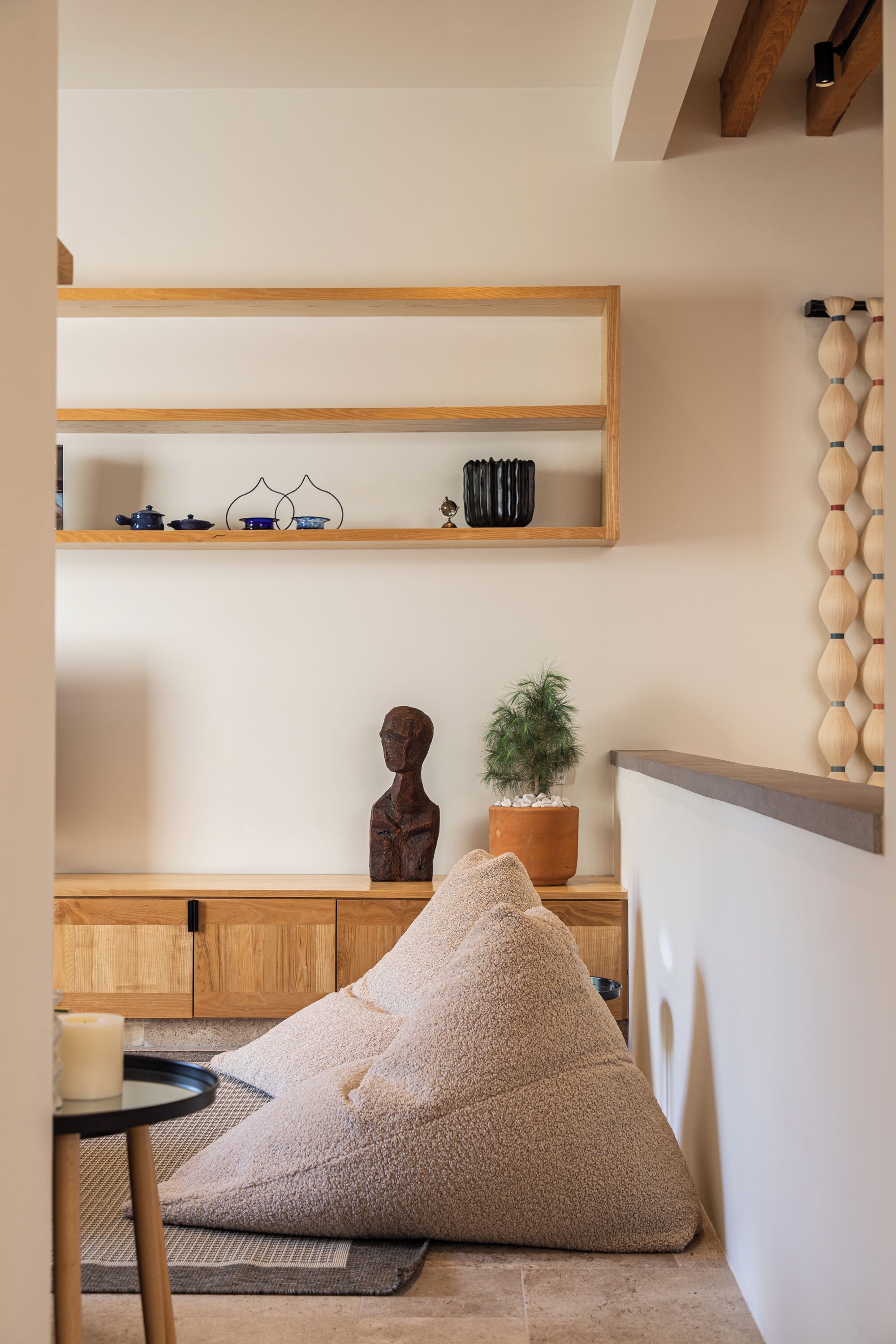 A cozy living area with a wooden bench, a beige bean bag, a small table with a candle, and a potted plant.