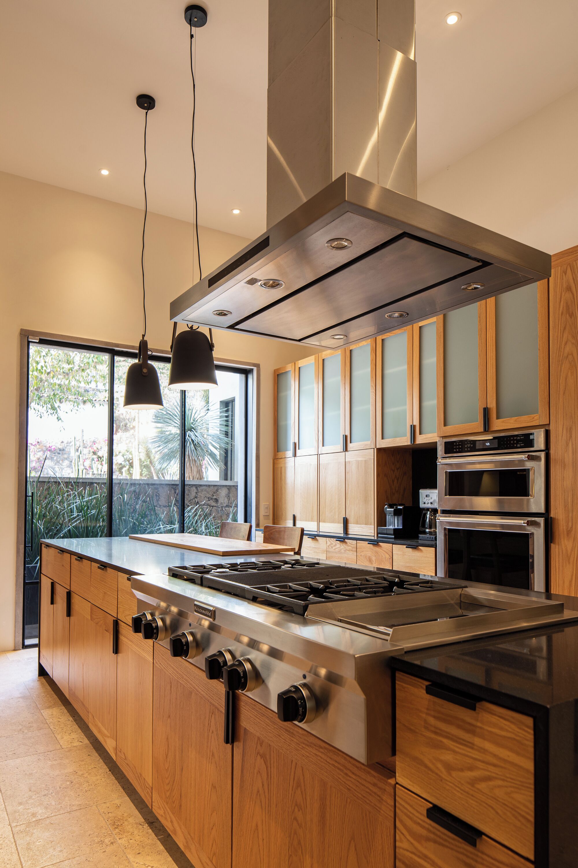 Une cuisine moderne dotée d’un îlot central, d’appareils électroménagers en acier inoxydable, de meubles en bois et de grandes fenêtres.